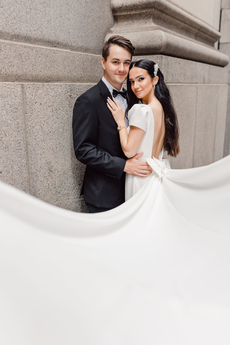 Bride and groom embracing beside classical stone architecture