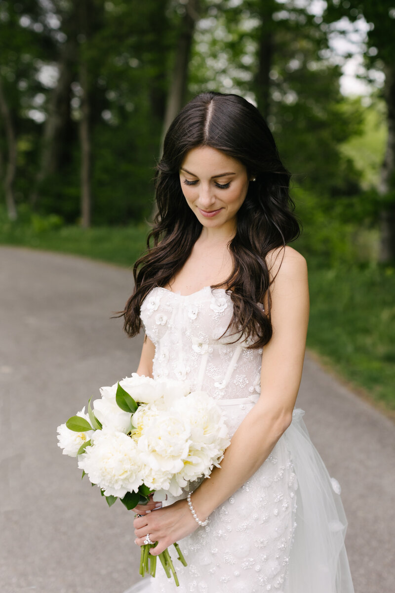 Bride holding a white bouquet on a tree-lined path