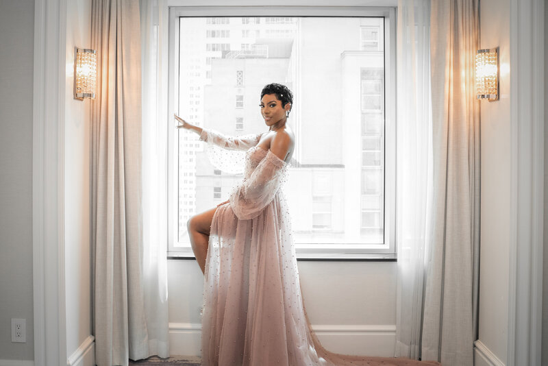 Bride in a blush gown posed beside a bright hotel window